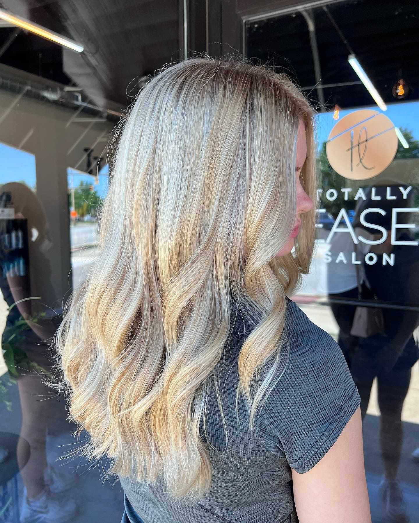 Woman showcasing her blonde balayage hairstyle at a salon.