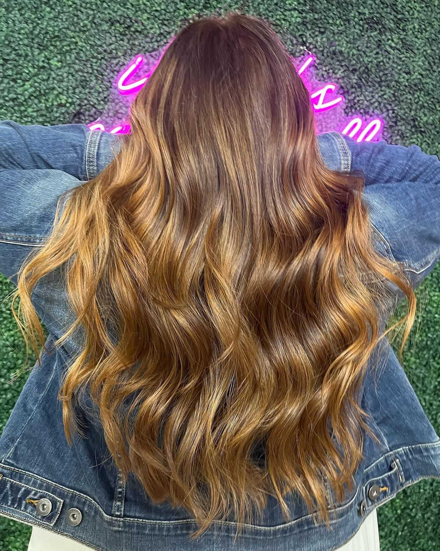 Person with long, wavy brown hair and a denim jacket, neon sign above.